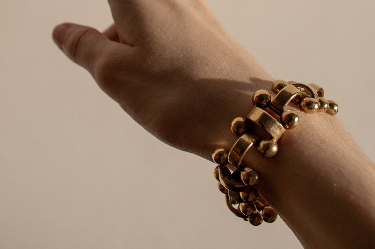 an outstretched hand against a beige background, wearing a chunky gold bracelet