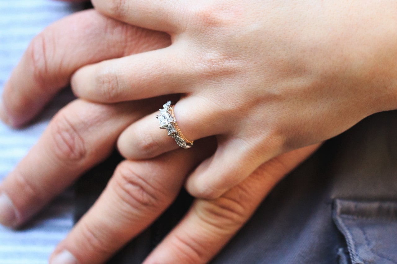 a couple’s hands intertwined – the woman donning a mixed metal three stone engagement ring