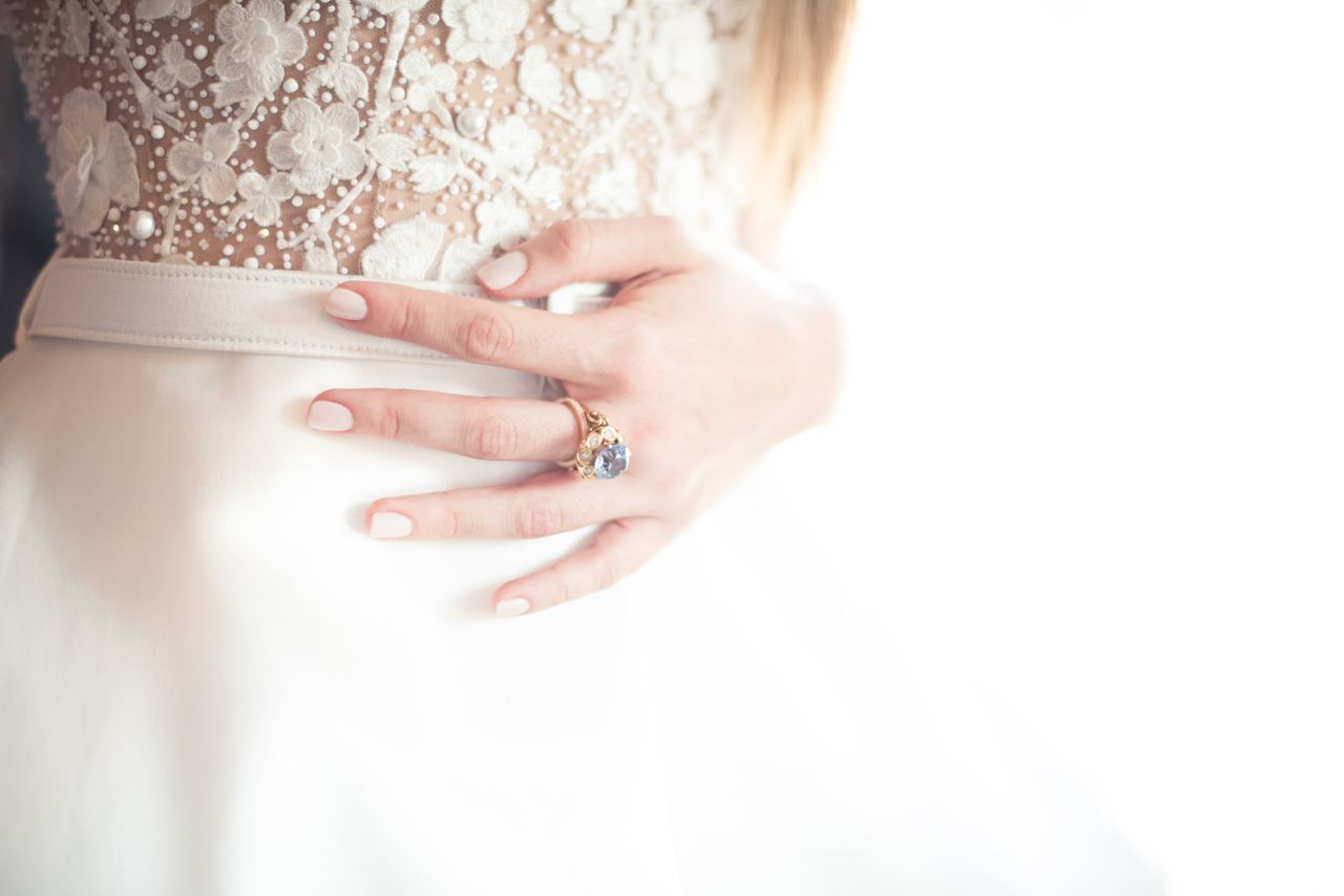 A bride stands in front of a window before the wedding, wearing a blue topaz ring.