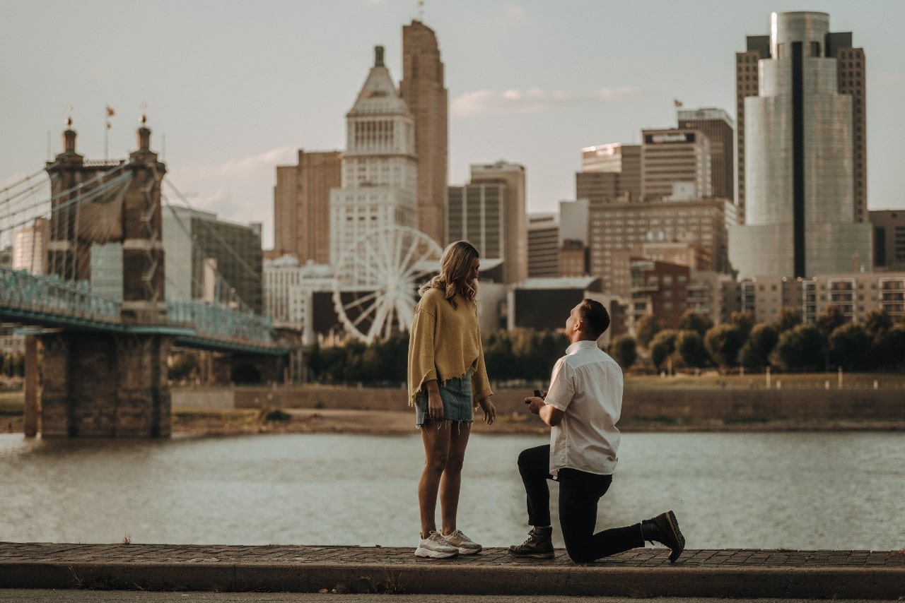 a man proposes to his girlfriend on a bridge in front of a bustling city.