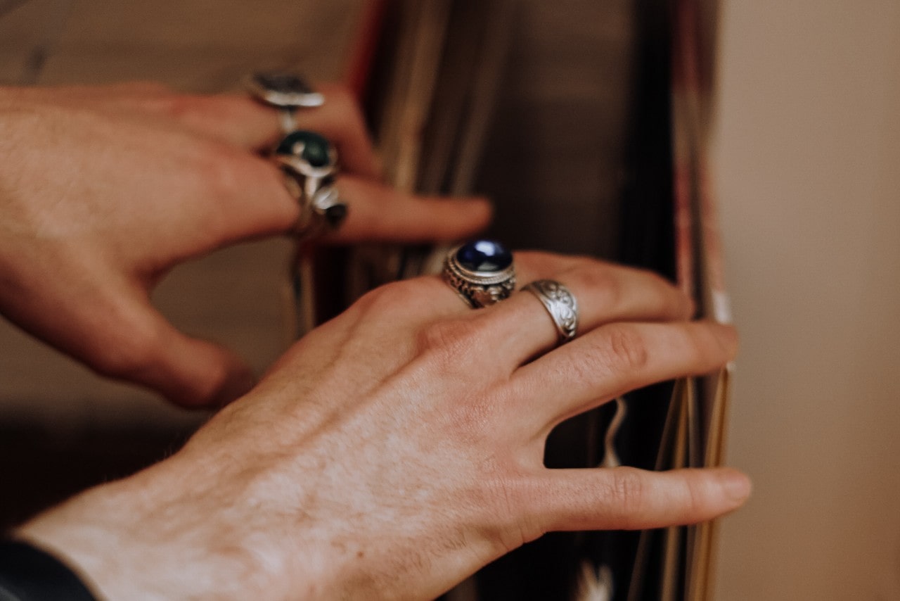close-up image of hands looking through records and wearing several white gold rings, some featuring sapphires