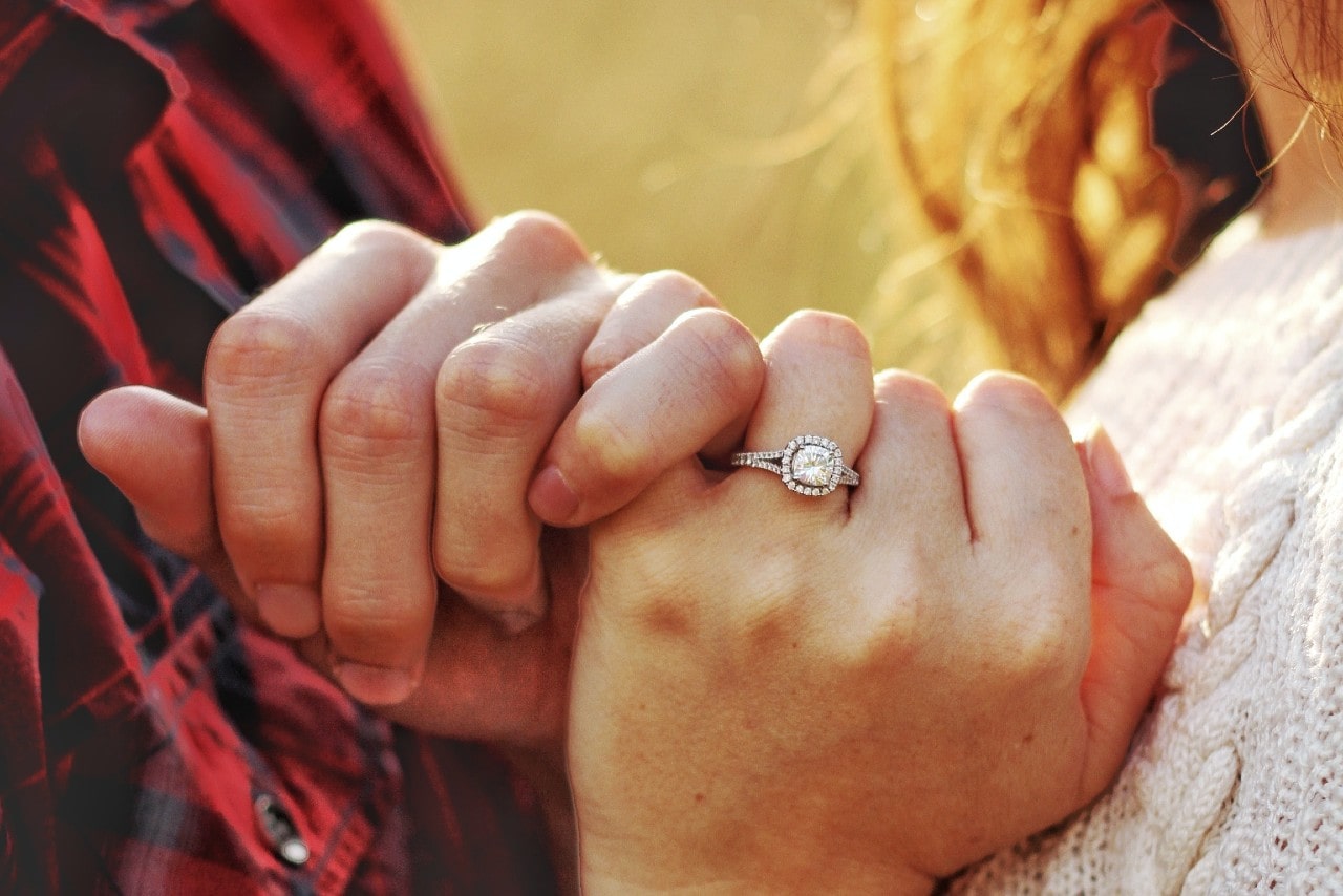 A couple intertwining pinking, the woman wearing a halo diamond engagement ring