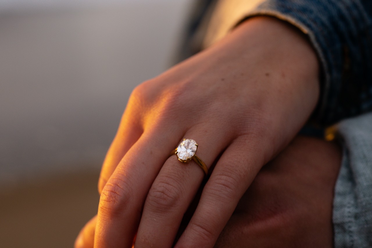 A couple holding hands, the woman wearing a yellow gold, oval cut diamond ring