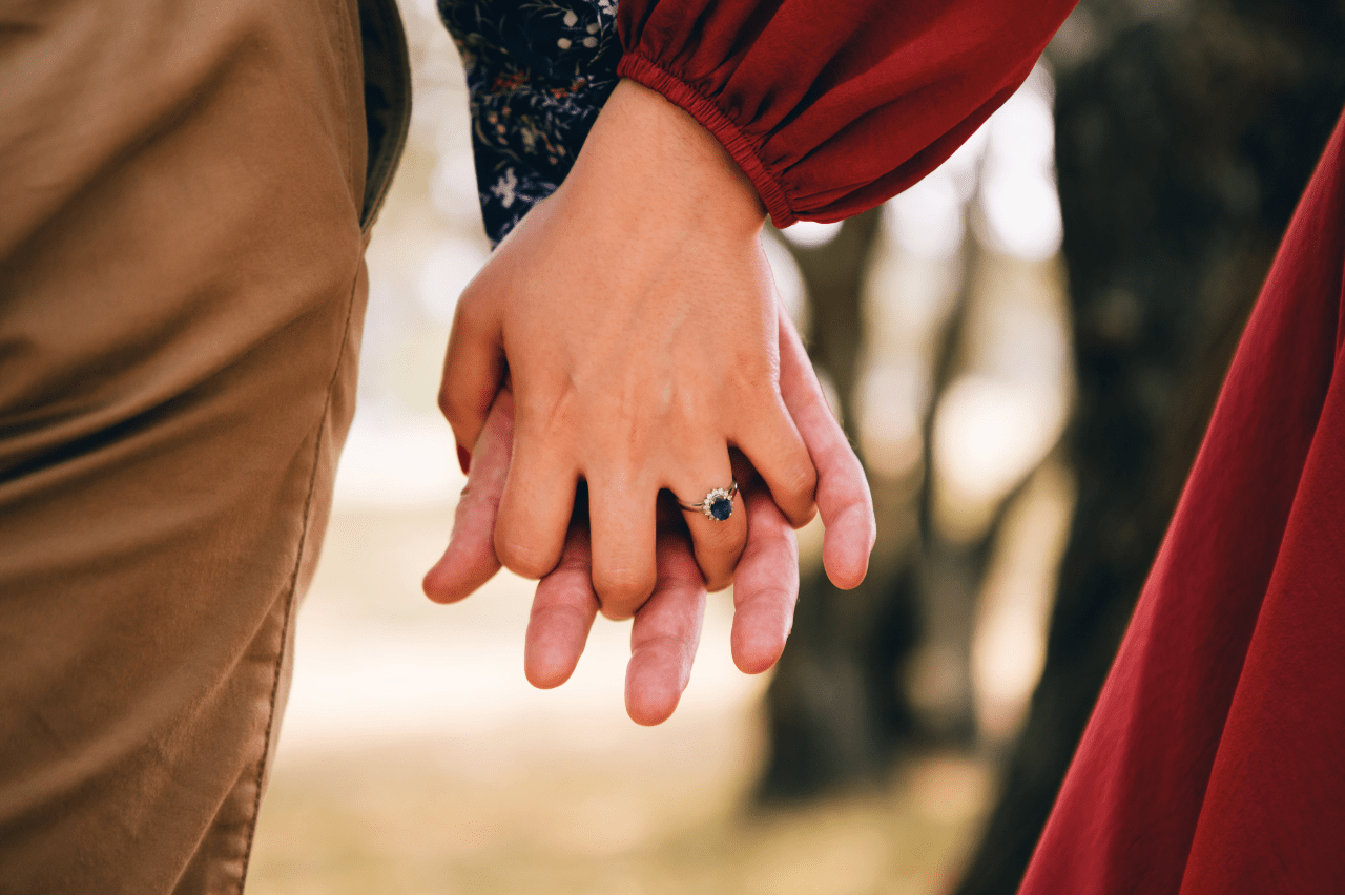 A couple holding hands, the woman wearing an oval cut sapphire engagement ring