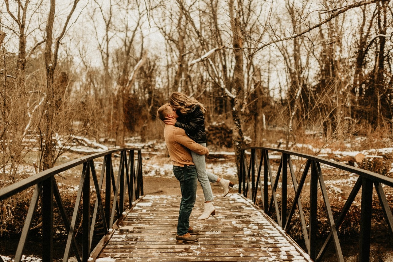 A couple embraces on a bridge on a cold fall day.