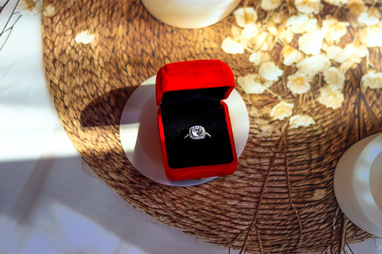 A close up of a halo white gold engagement ring inside the black and red velvet jewelry box on top of the tupperware.