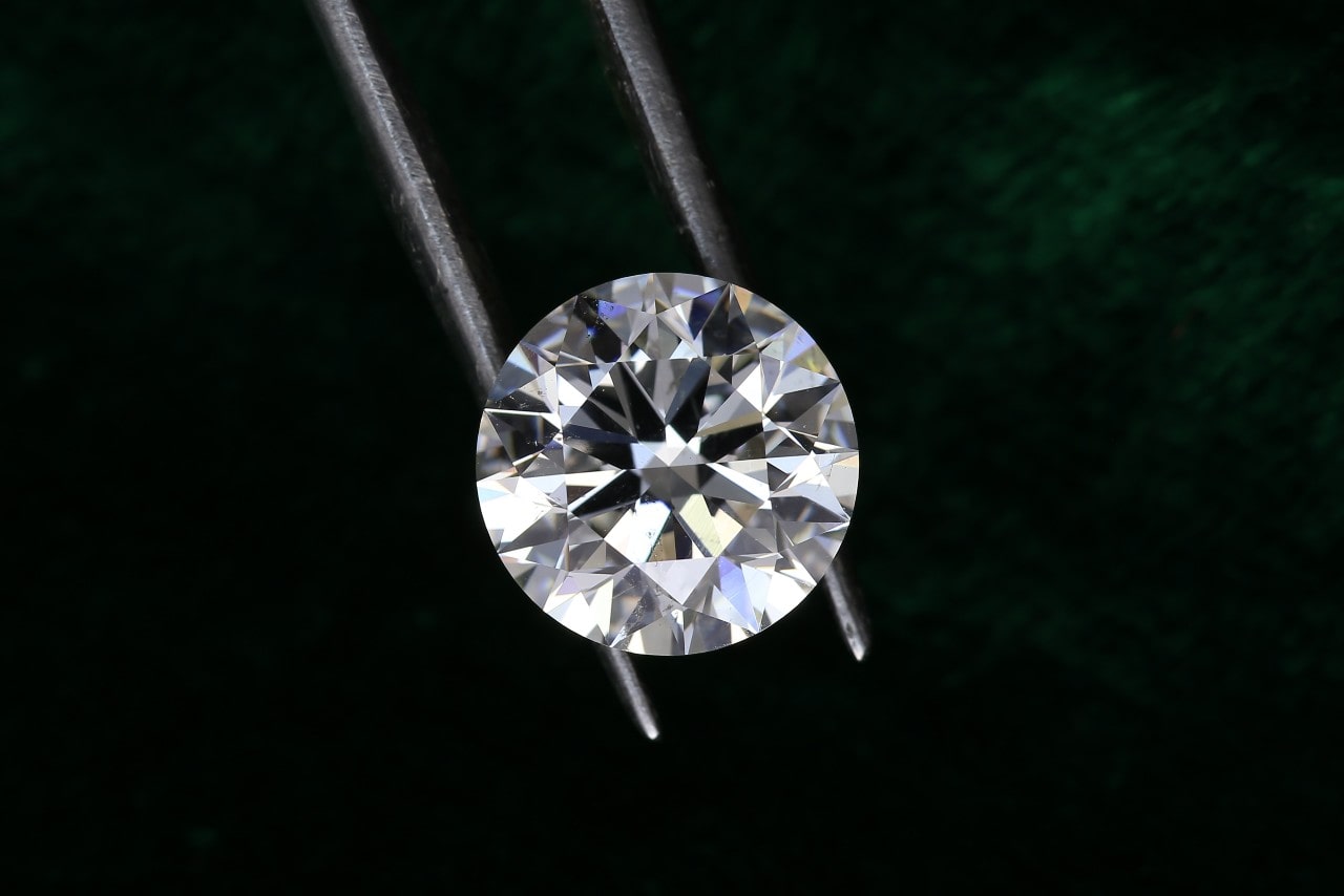 A gemologist carefully holds a round-cut lab-grown diamond against a dark background