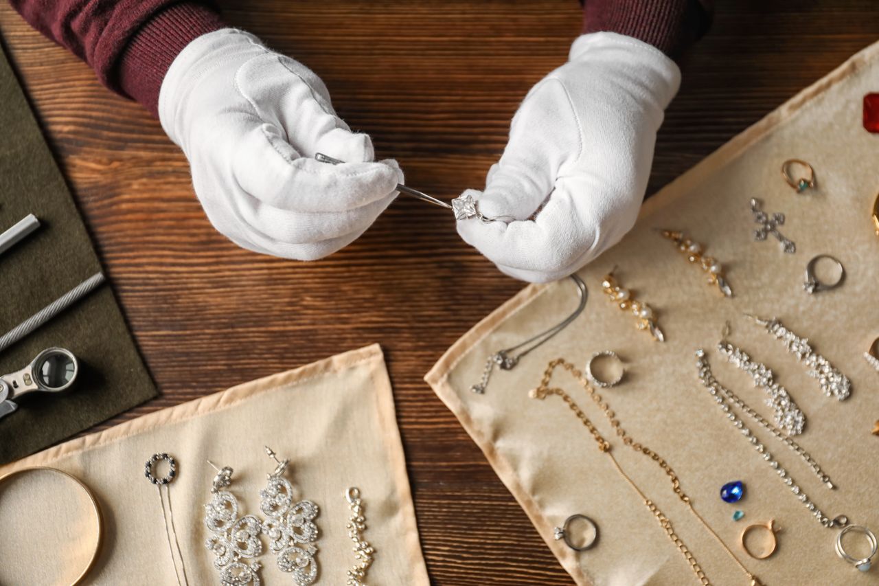 A jeweler cleans her collection of jewelry on her workspace while wearing gloves