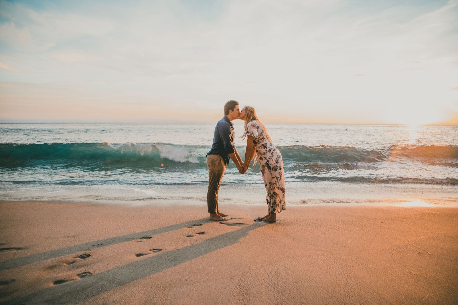 An adventurous couple kisses on a beach during low tide as the sunsets in the background