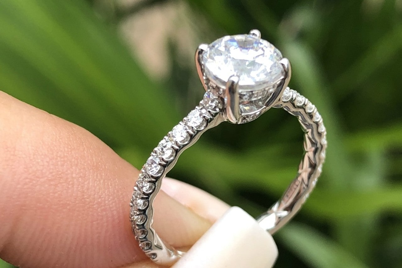 A woman with acrylic nails holds her side stone, hidden halo diamond ring while on a walk outside