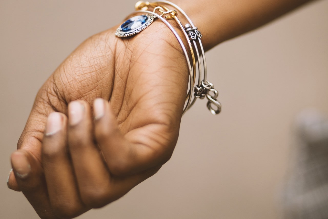 A close-up of a person’s wrist adorned with bangles, one of the bangles containing a large blue gemstone.