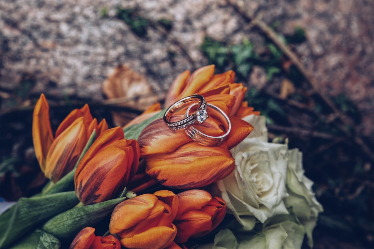 Round cut engagement ring and silver wedding band sitting atop a bouquet of flowers