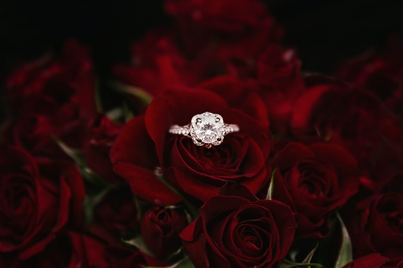 Round cut engagement ring sitting atop a bouquet of roses