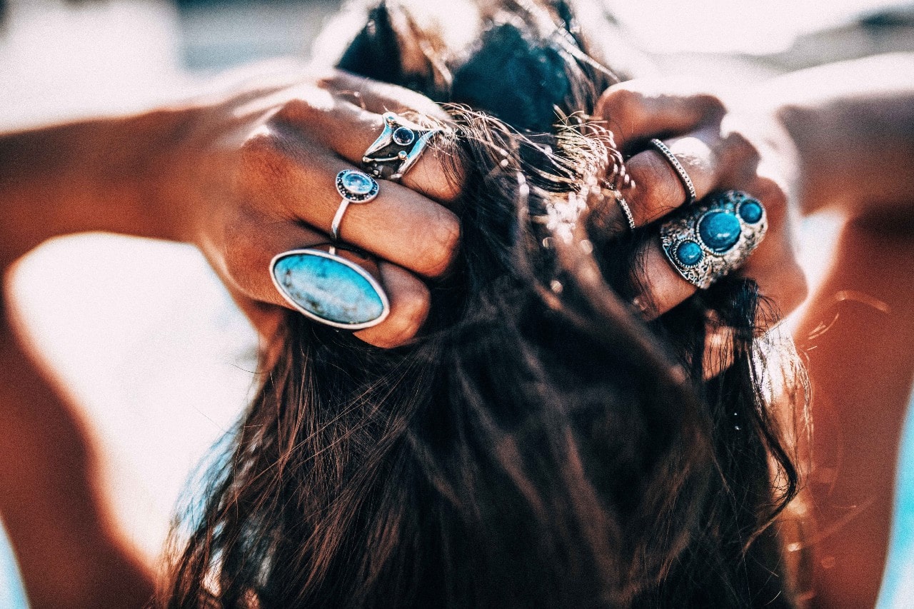 Woman holding back her wet hair wearing a plethora of turquoise fashion rings.