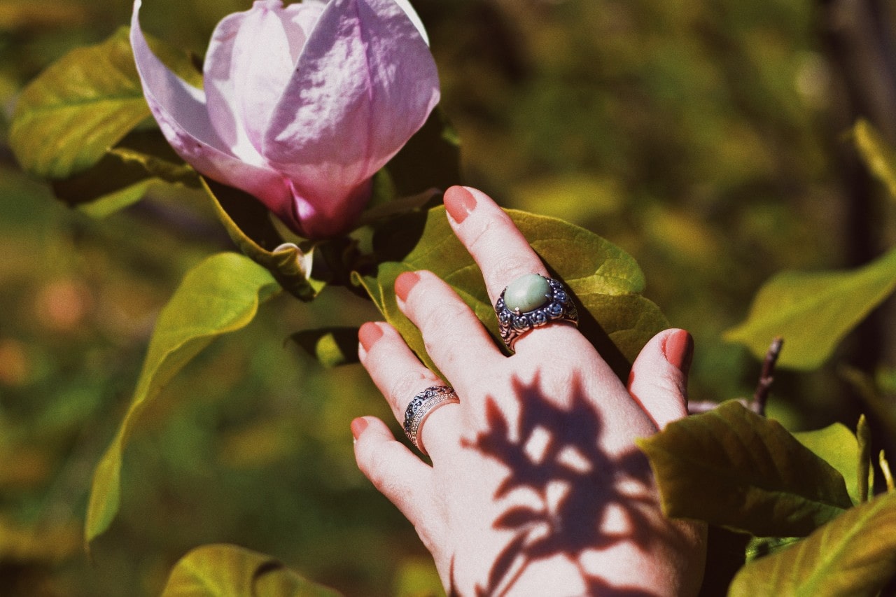 Person with a fashion ring stack reaching for a purple flower.