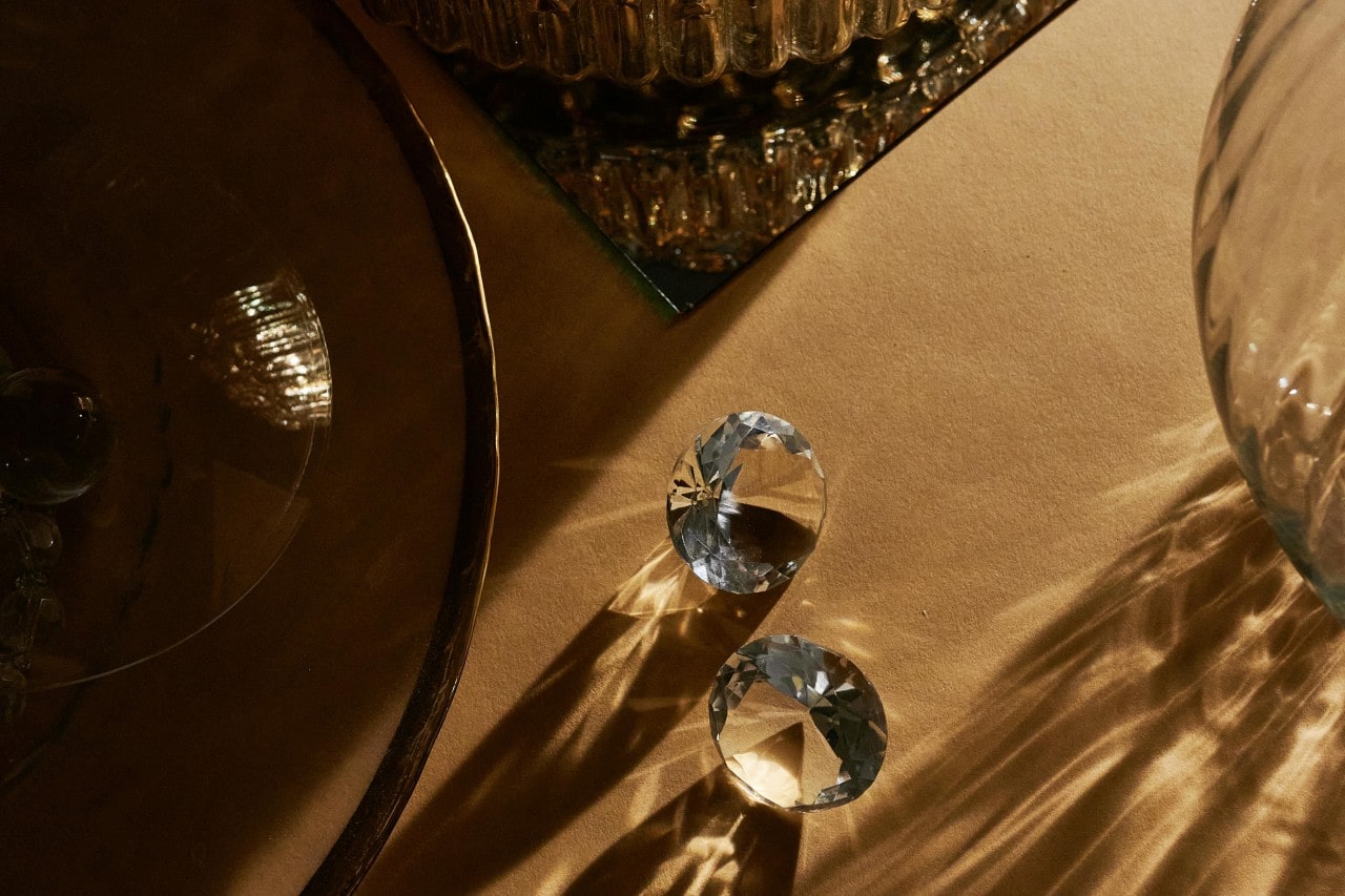 A close-up of two round cut diamonds on a sunlight surface beside two glass vases.