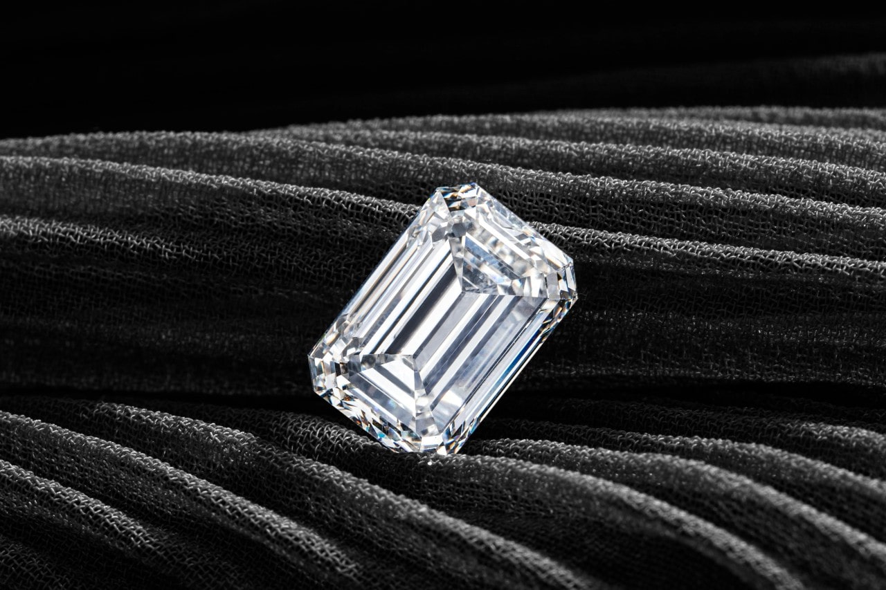 A close-up of an emerald cut diamond on a grey fabric.