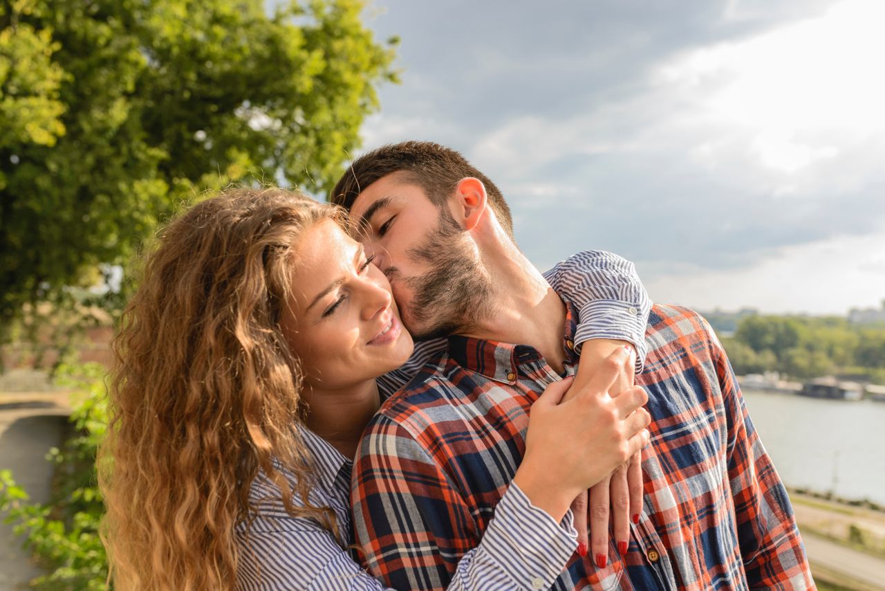 Two married people sharing a hug and kiss whilst overlooking a river.