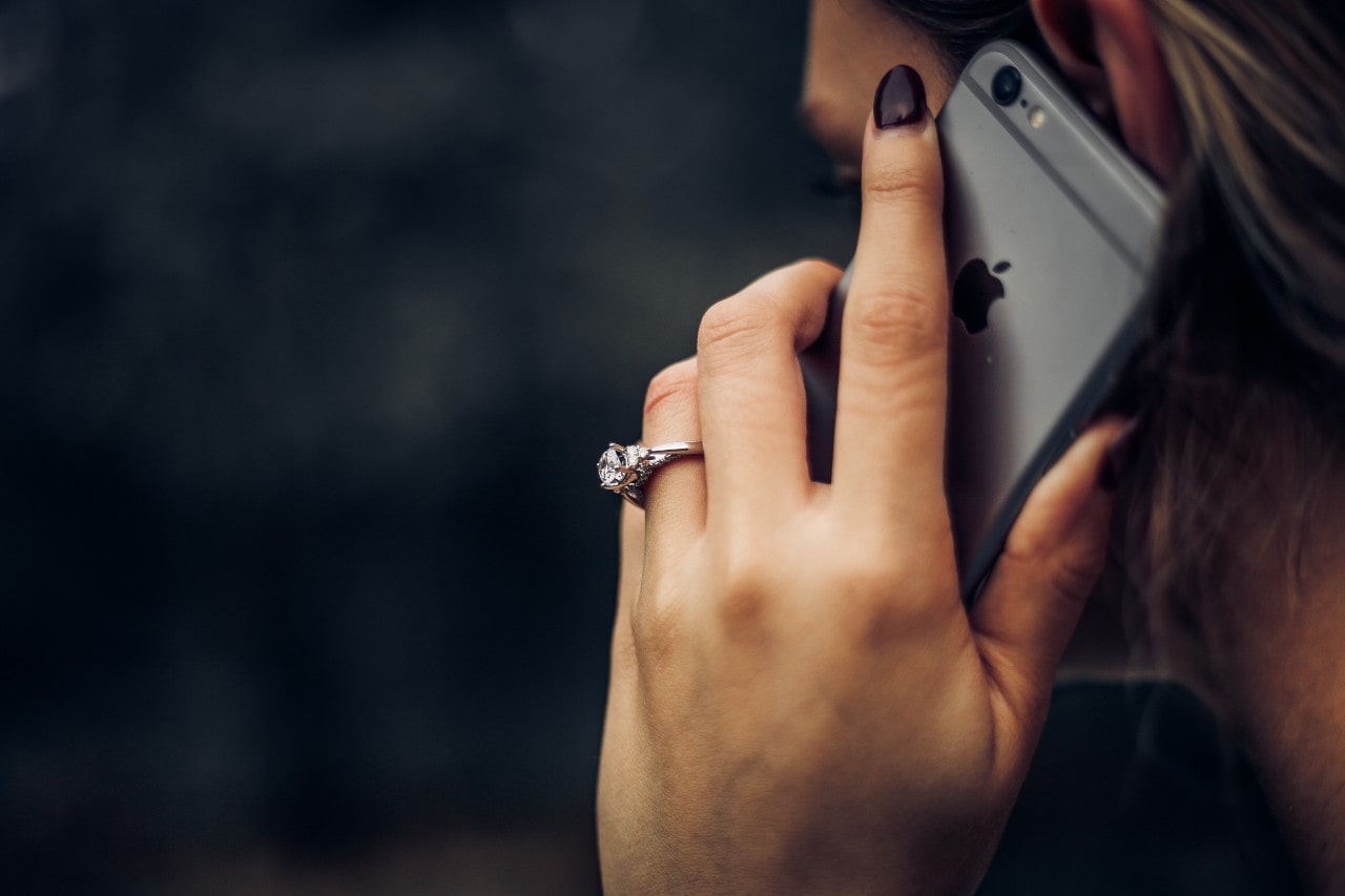 Woman on the phone, her three stone engagement ring prominent in the center.