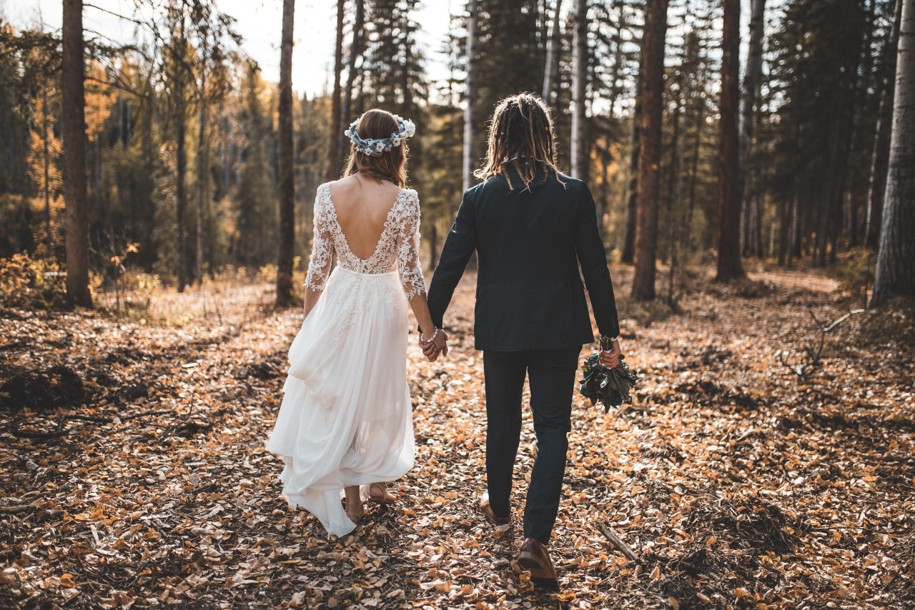 Bride and groom seen from the back as they walk further into autumnal woods.