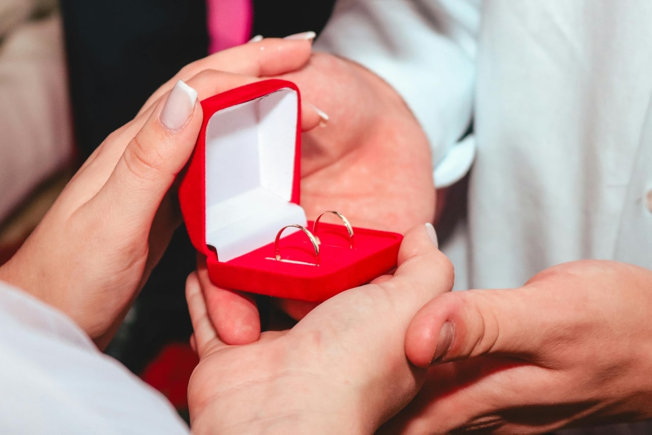 A man giving a woman a red jewelry box open with delicate gold hoop earrings inside.
