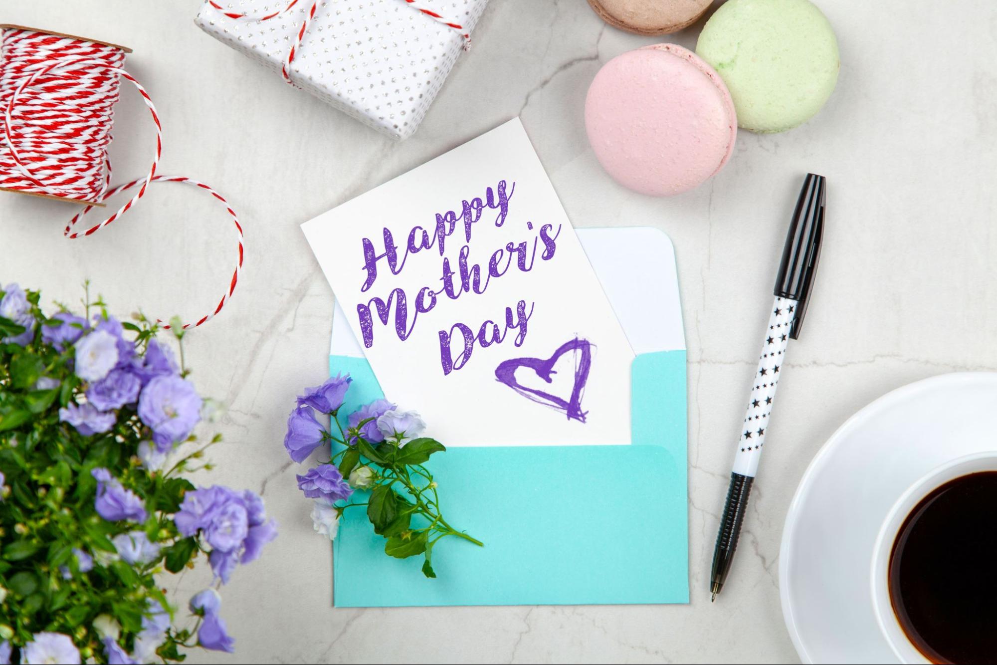 A Mother’s Day card sits among a pen, flowers, macaroons, and a wrapped gift.