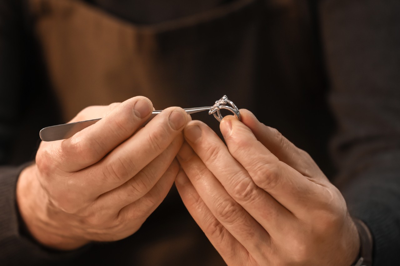 Close up of a jeweler’s hands inspecting a diamond ring with a metal tool.