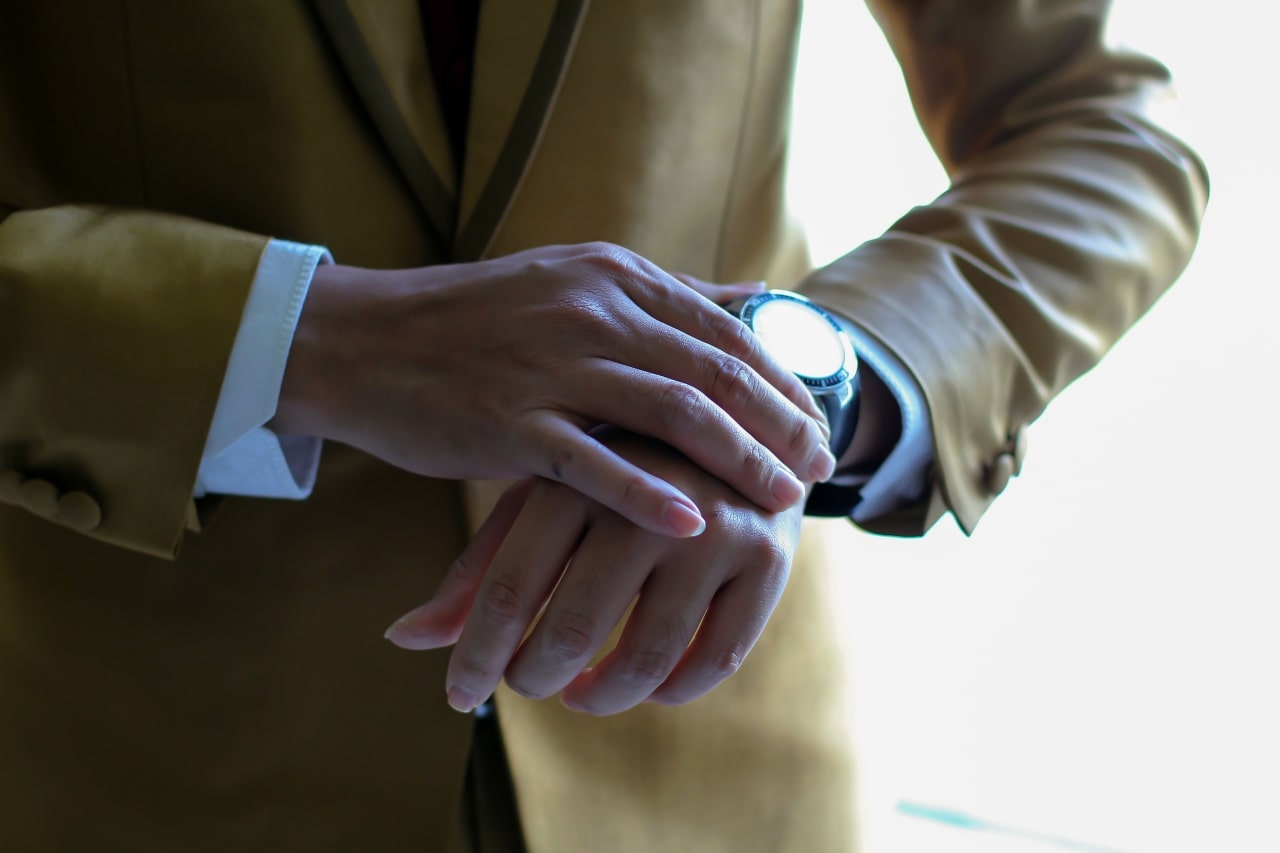 Close up image of a person in a tan suit adjusting their watch