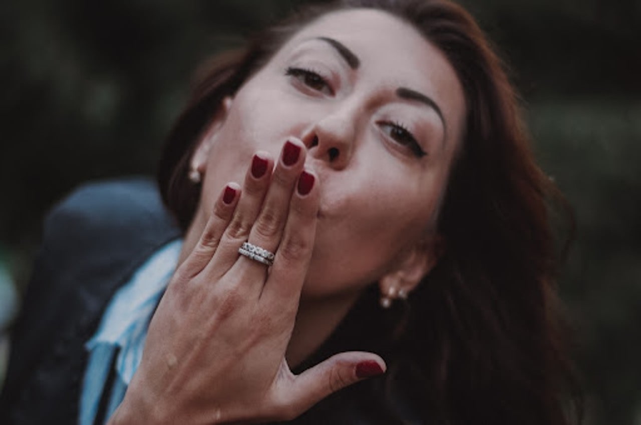 a woman bundled up blows a kiss while wearing white gold fashion rings.
