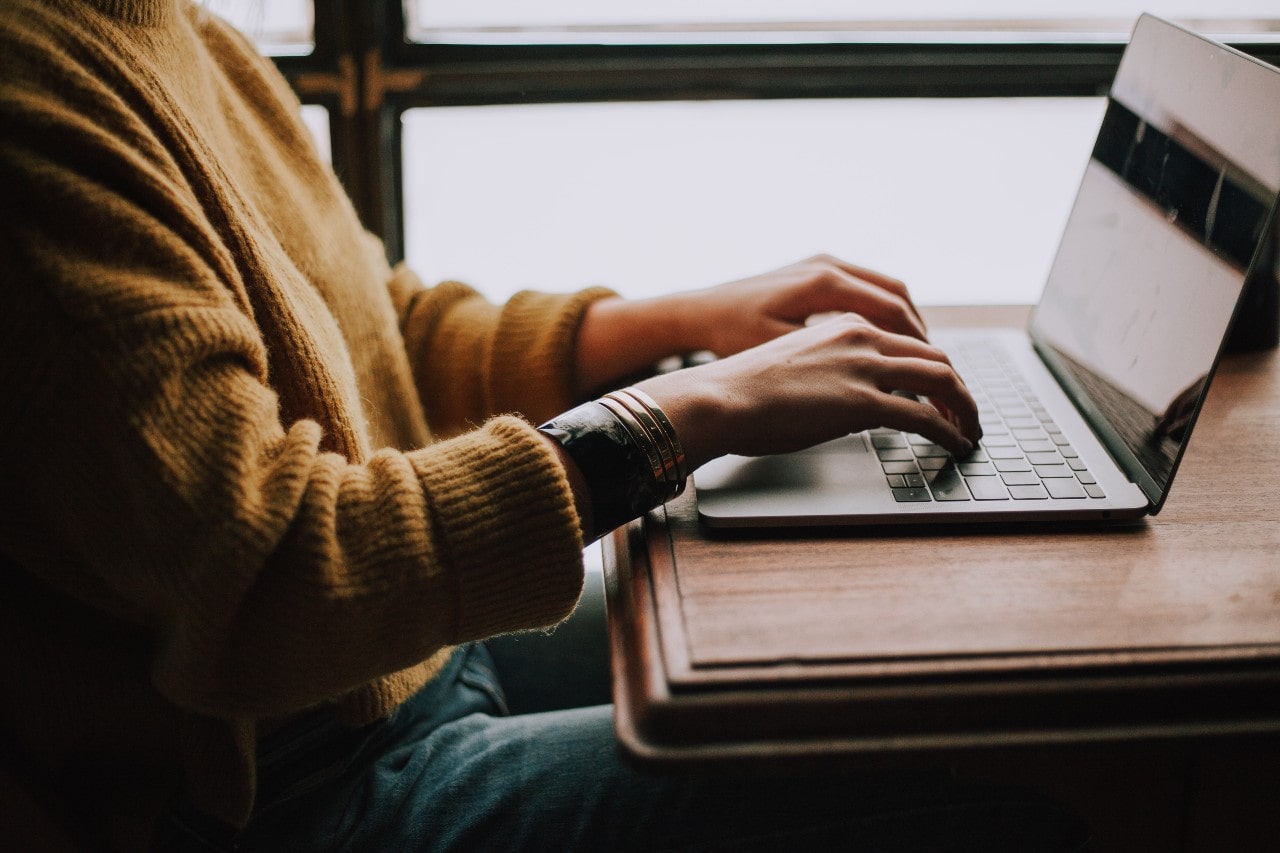 A woman doing work on a laptop while wearing a yellow sweater with bangles.