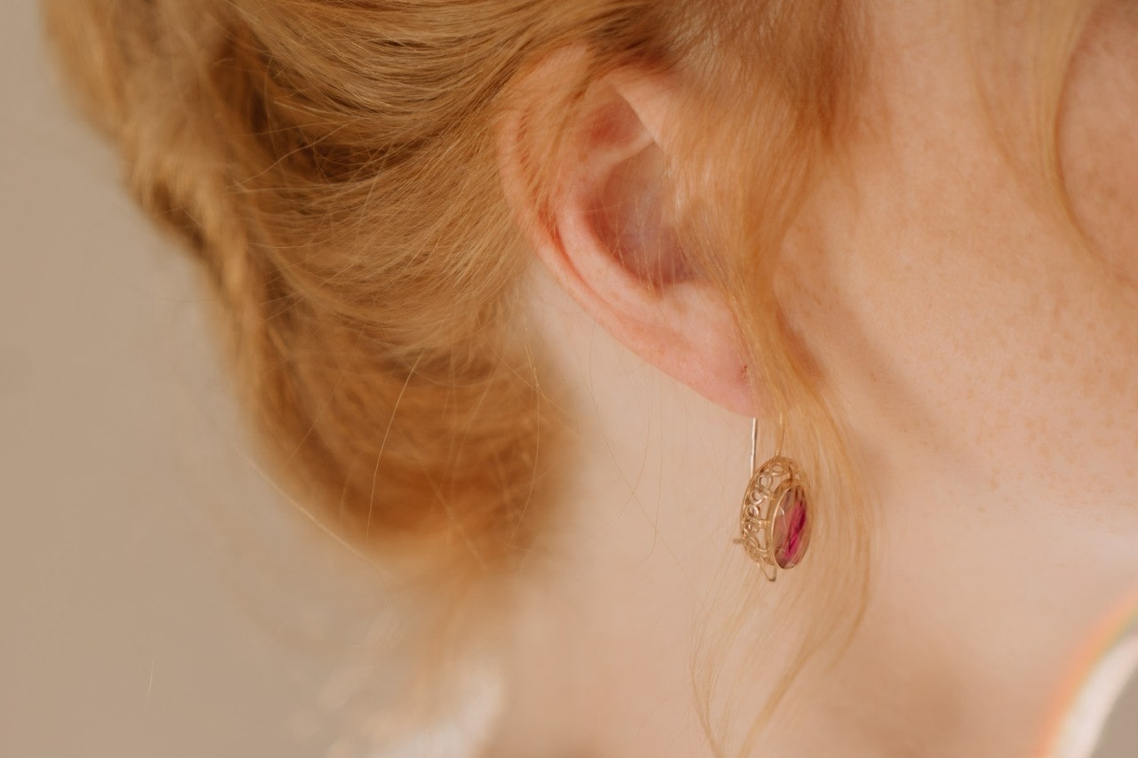 A redhead woman wears a ruby drop earring from Fana.
