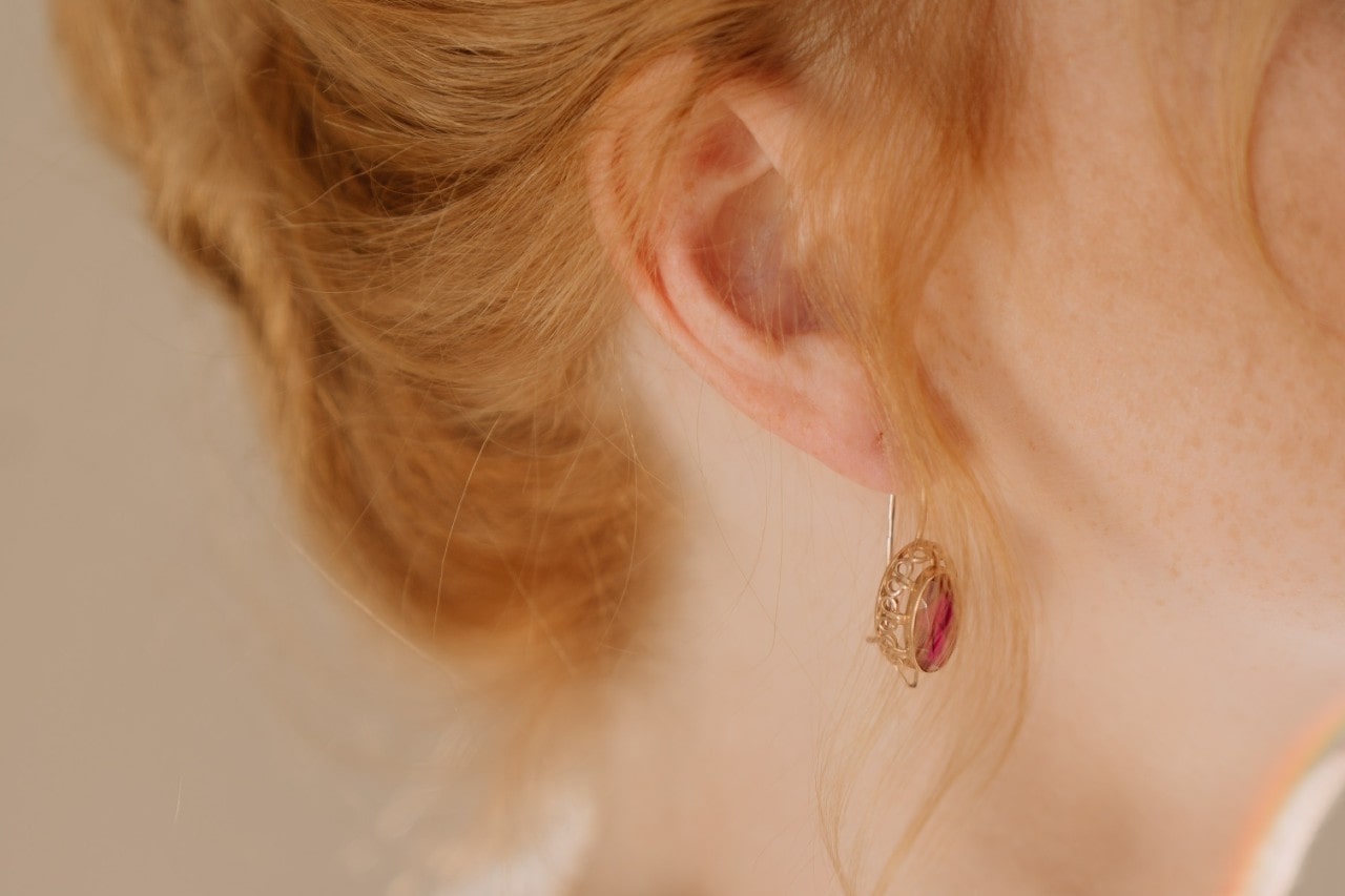 A redhead woman wears a ruby drop earring from Fana. A redhead woman wears a ruby drop earring from Fana.