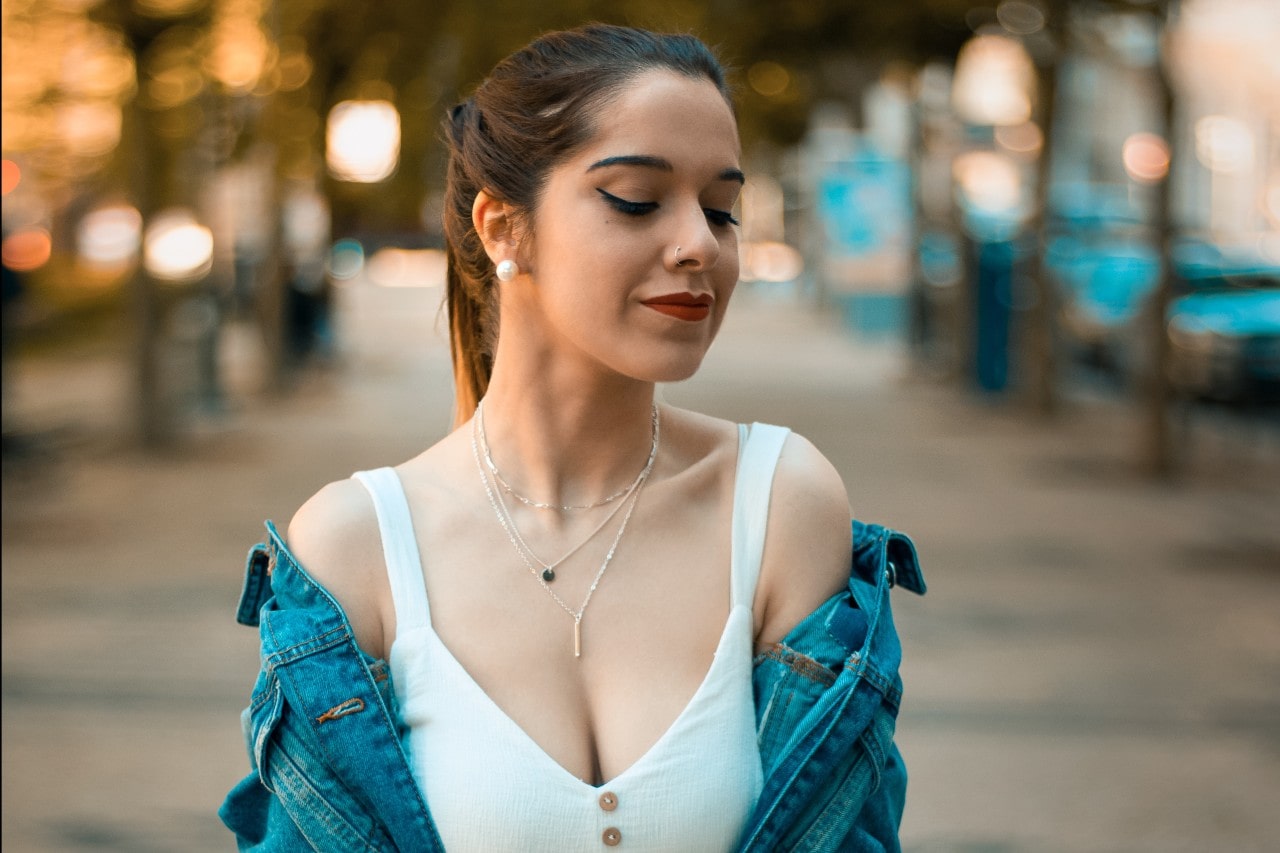 A woman in casual attire wearing three necklaces from Fana and pearl earrings walking down the street.