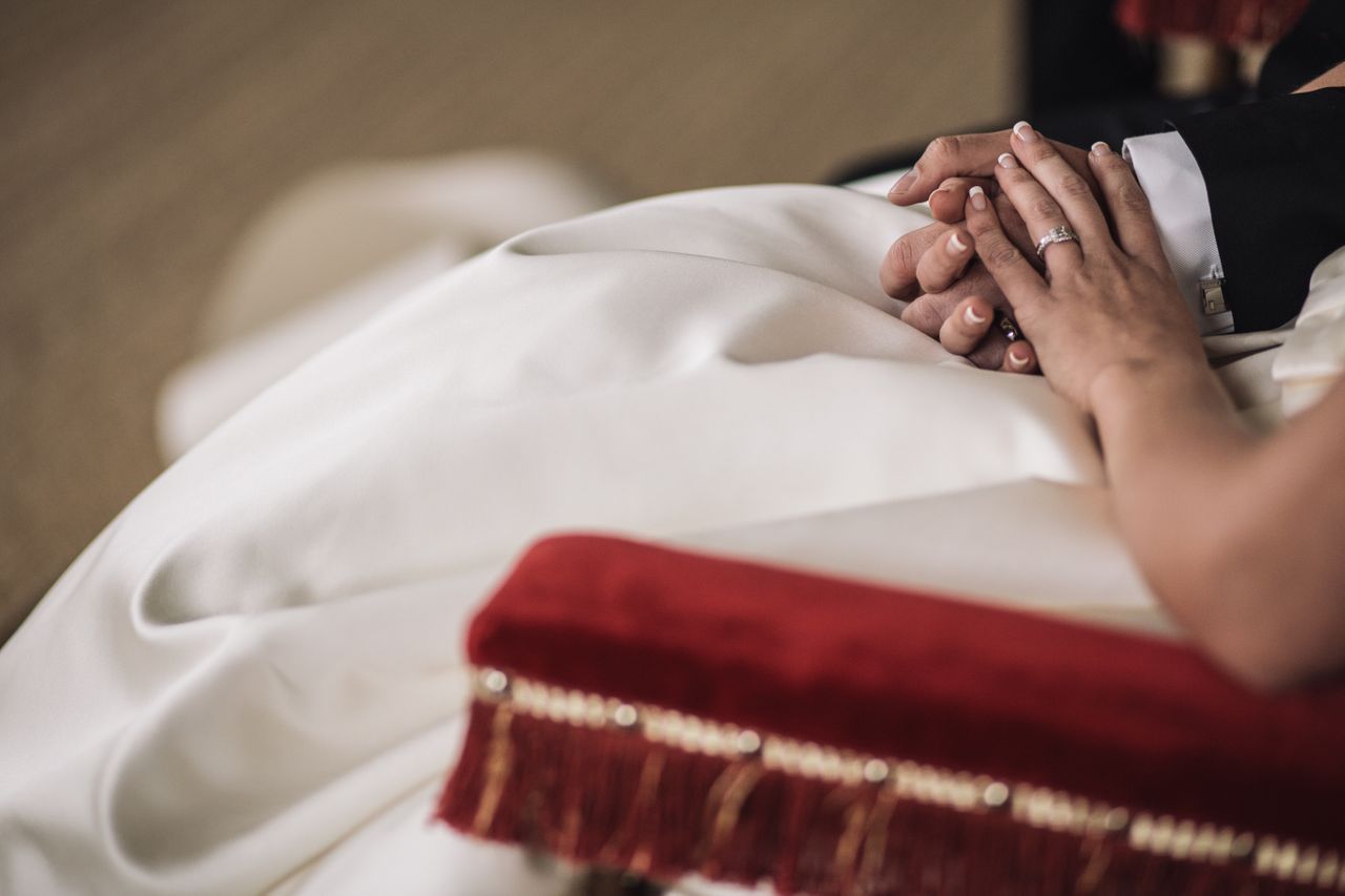 a bride and groom hold hands and sit together on a chair during their reception.