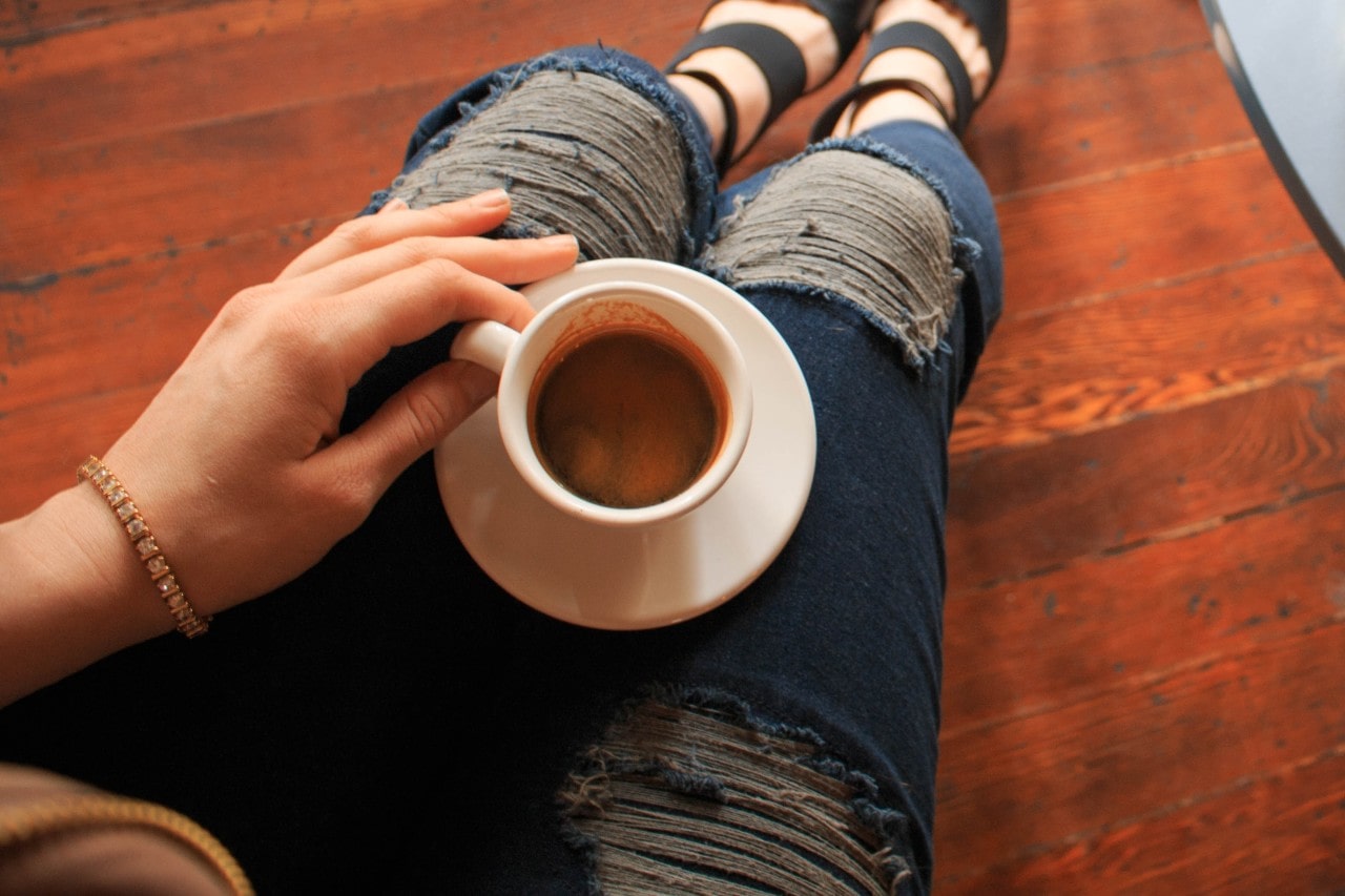 a woman sipping a latte sits on the floor while sporting a gold tennis bracelet.