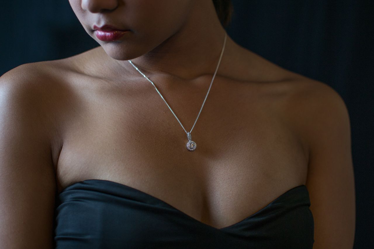 A woman in a black formal dress wears a solitaire diamond necklace.