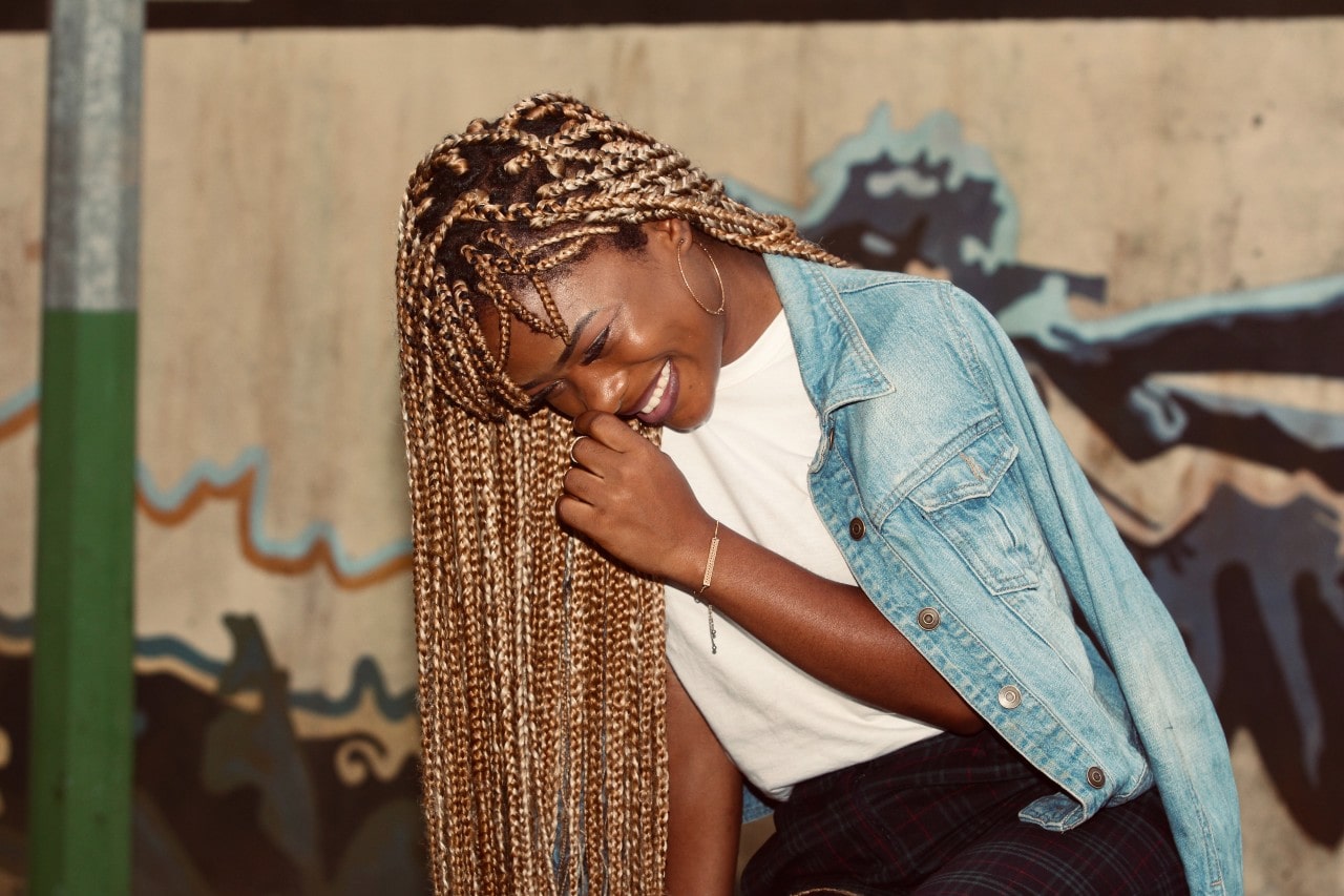 a woman doubled over in laughter, wearing gold jewelry and a denim jacket