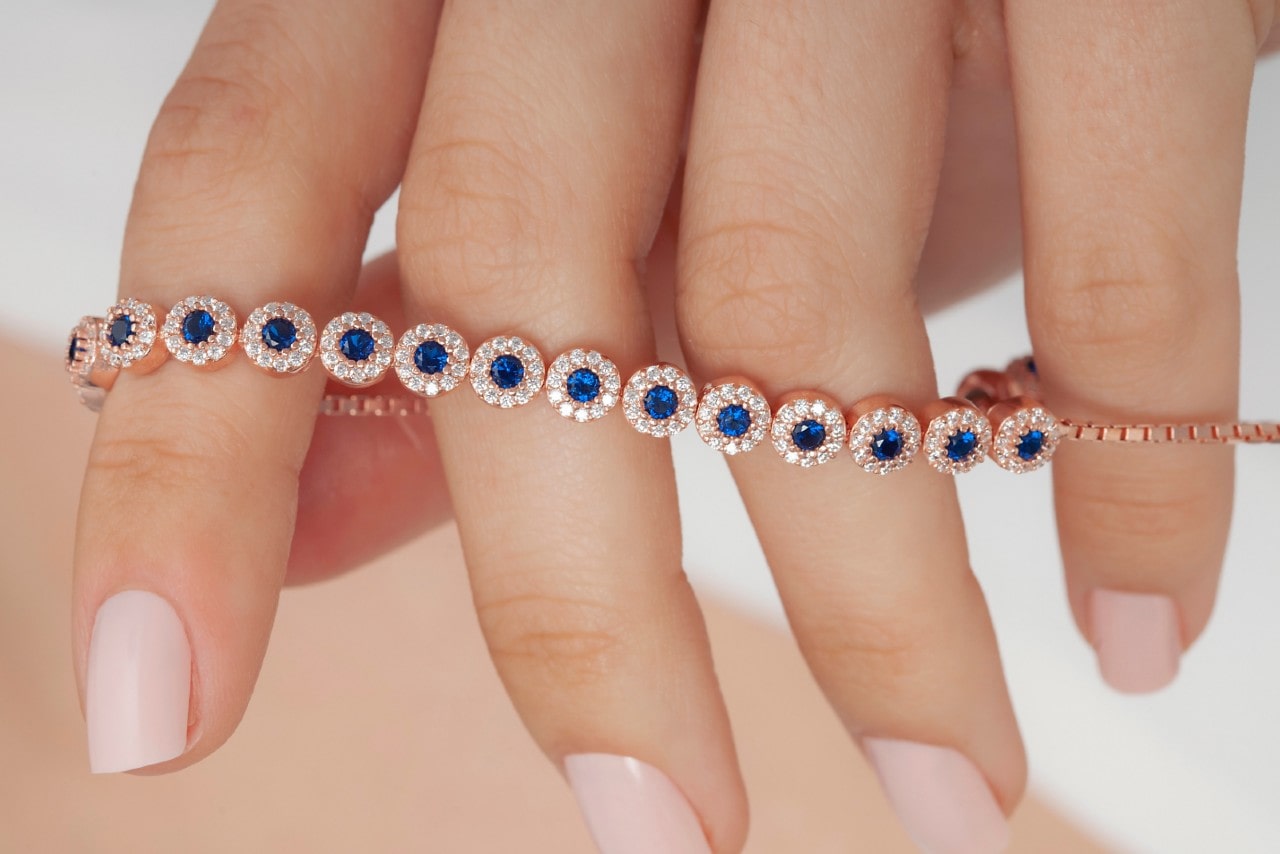 a hand holding a rose gold line bracelet featuring halo set sapphires