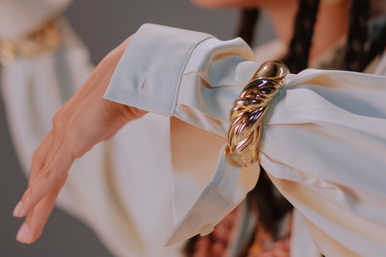 a woman’s arm clad in white blouse sleeve and a thick gold cuff bracelet