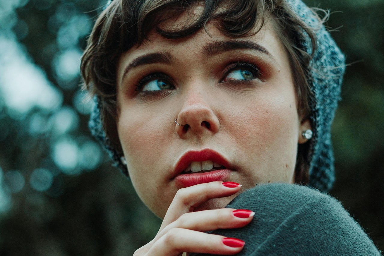 A close-up of a fashionable young woman in a knit hat, wearing bold diamond stud earrings.
