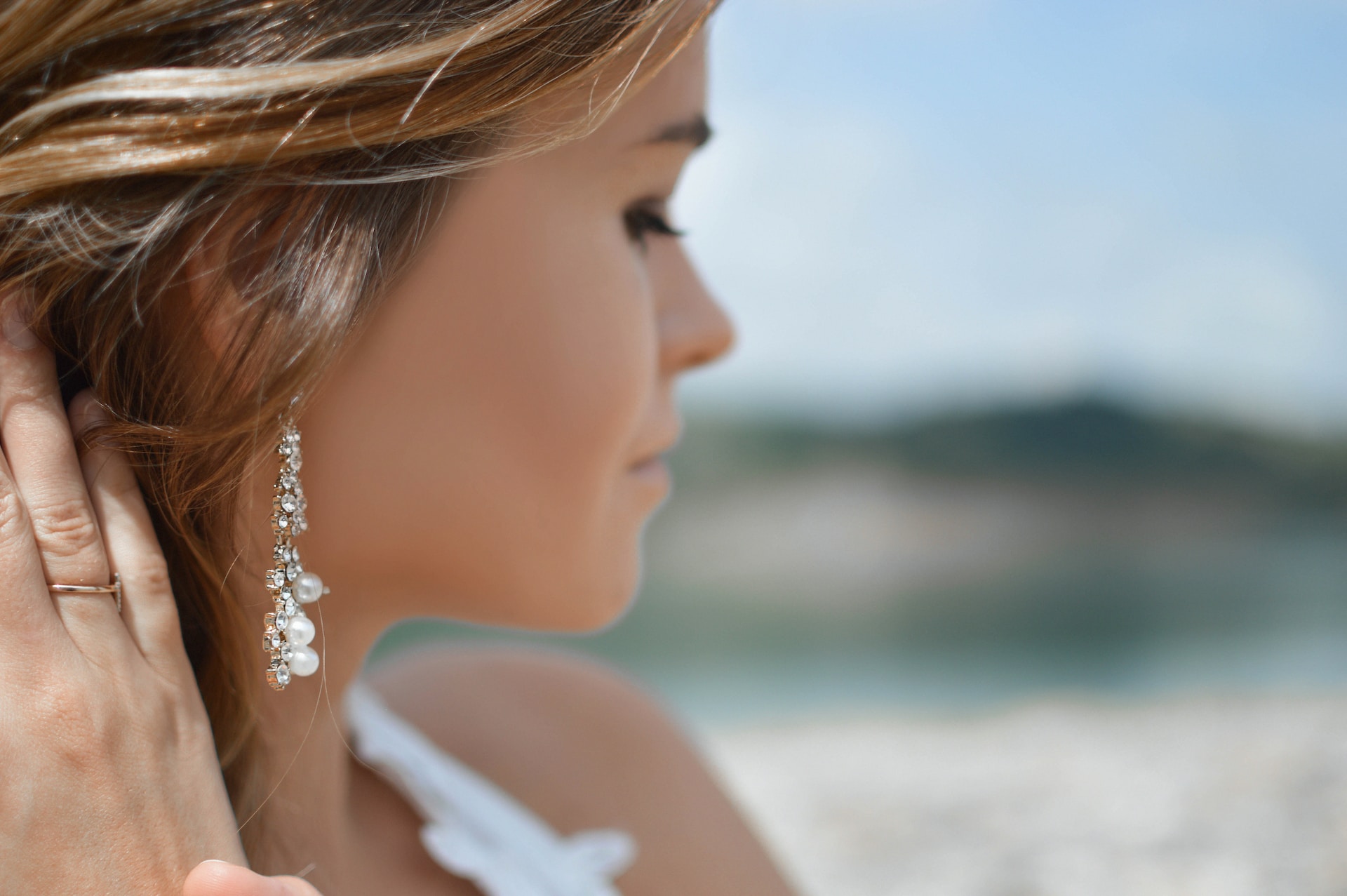 A close-up of a young woman’s profile, tucking her hair back to reveal a dazzling diamond and pearl drop earring.