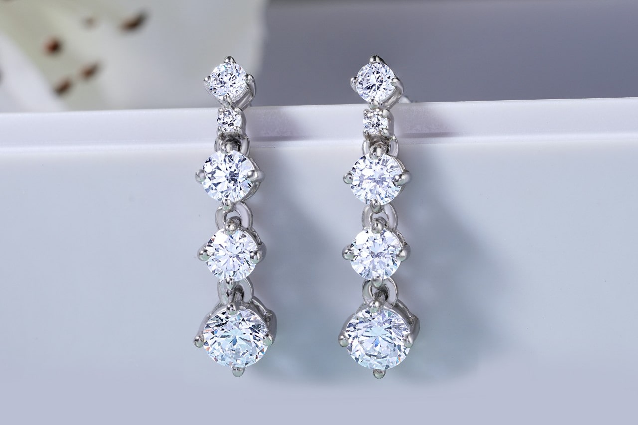 A close-up of a simple yet elegant pair of diamond chandelier earrings draped on a white display.