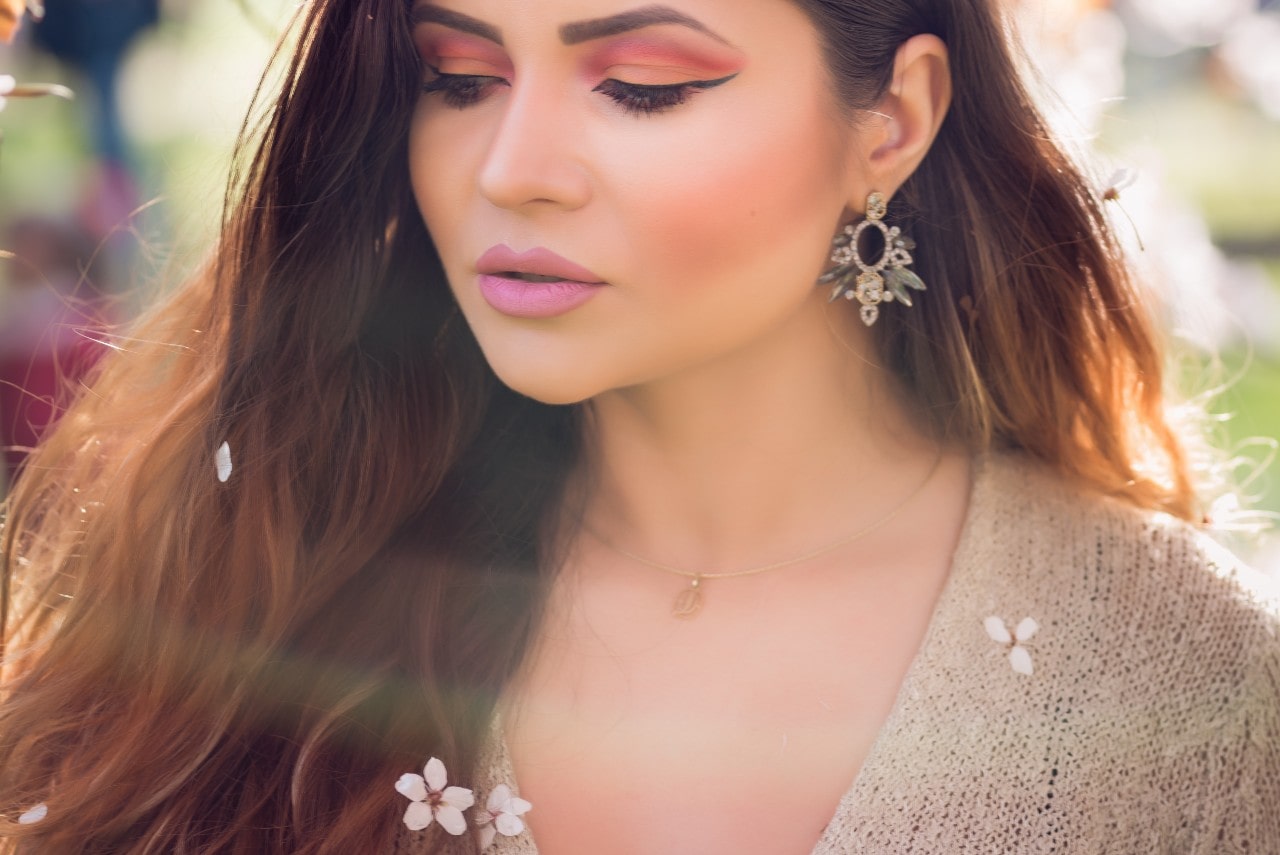 A model picks blossoms while wearing ornate gemstone drop earrings.