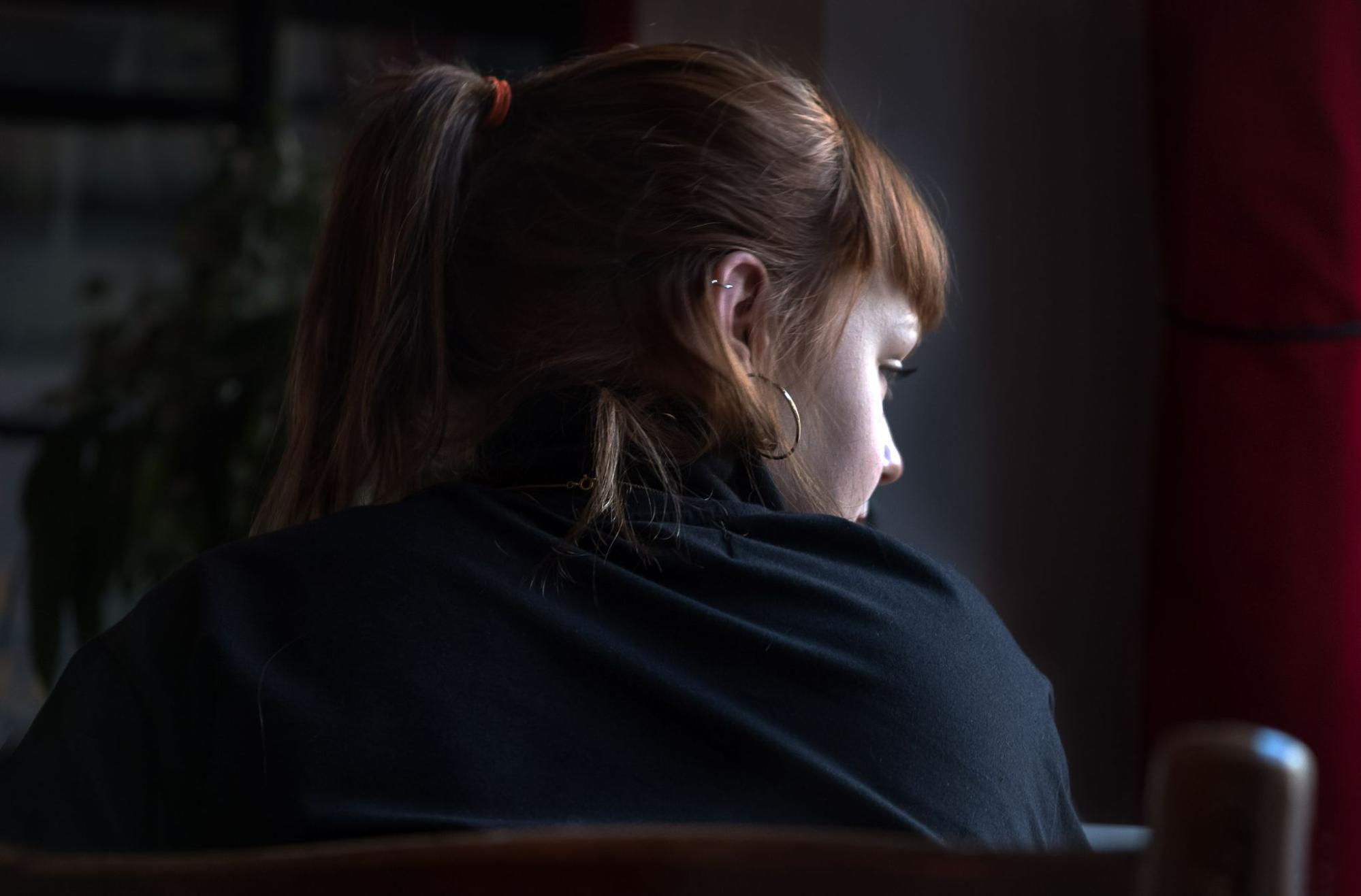 A posterior view of woman wearing hoop earrings in a library looks out the window