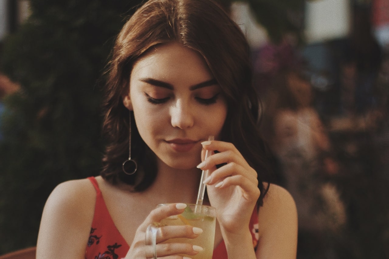 A woman sipping a lemonade while wearing drop earrings.