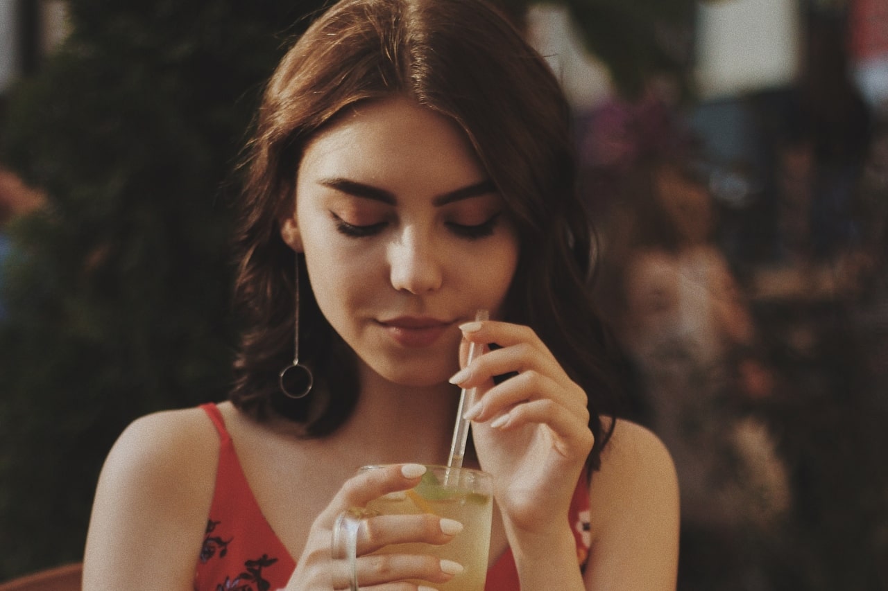 A woman sipping a lemonade while wearing drop earrings. A woman sipping a lemonade while wearing drop earrings.