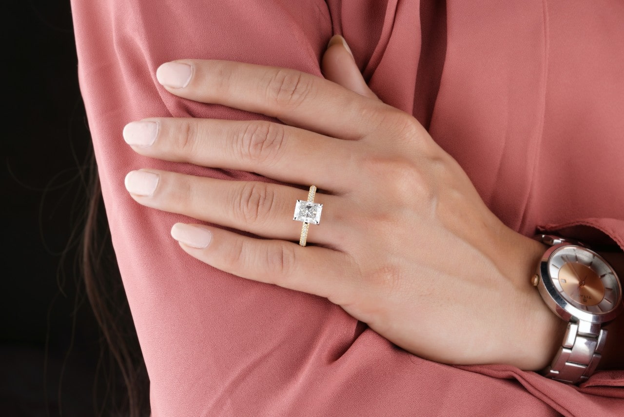 A close up of a woman’s hand, a princess cut yellow gold engagement ring with a side stone band on her finger. A close up of a woman’s hand, a princess cut yellow gold engagement ring with a side stone band on her finger.