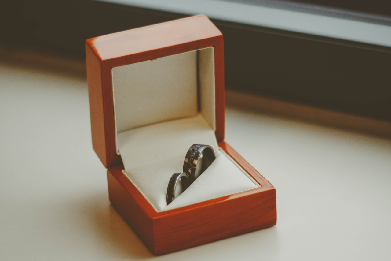 two black wedding bands sitting in a wooden box