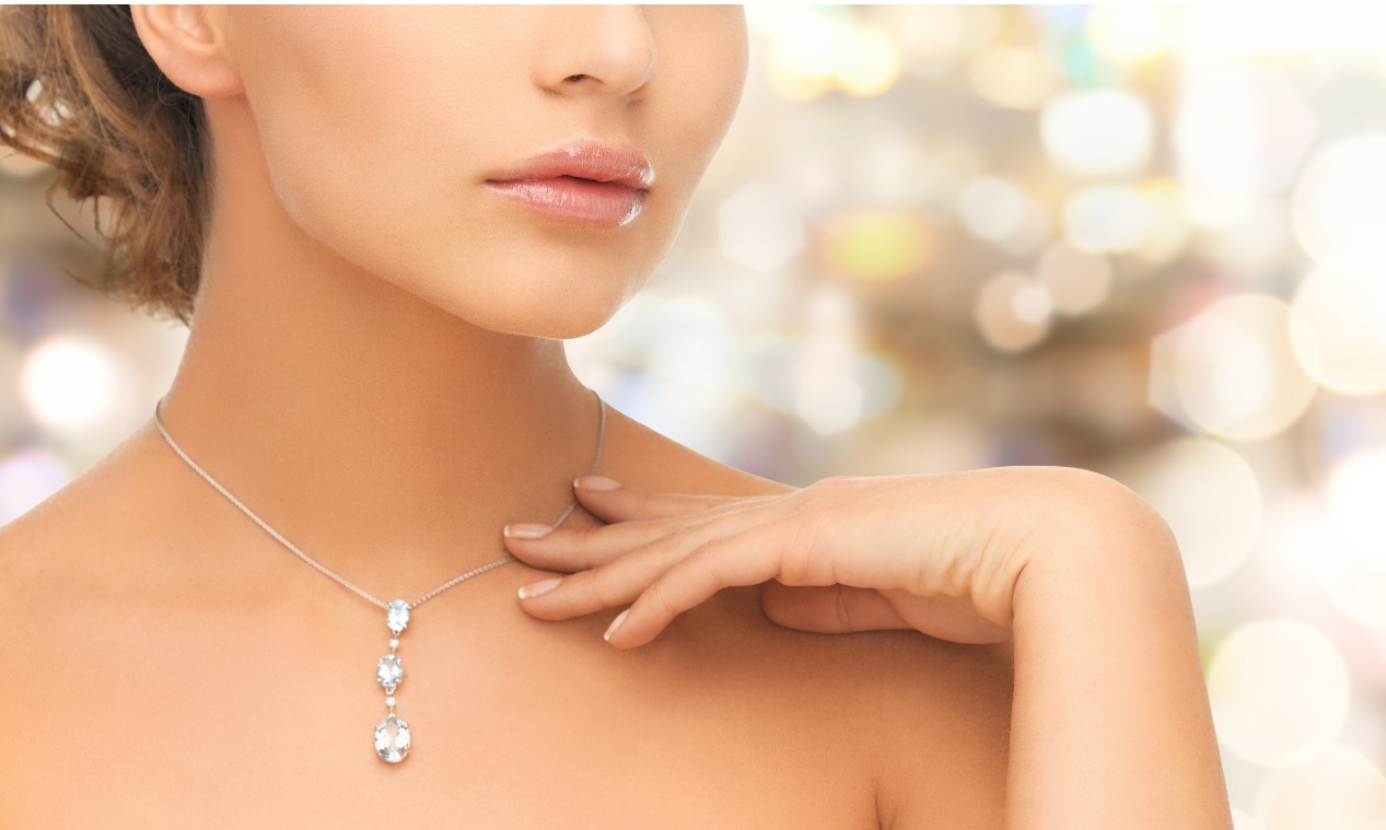 A close-up of a woman wearing a triple diamond drop necklace against a shiny bokeh background.