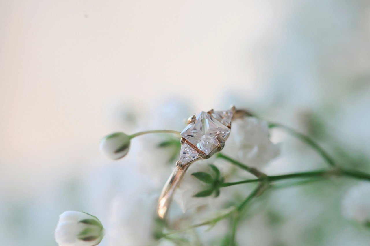 a three stone, princess cut engagement ring surrounded by tiny flowers